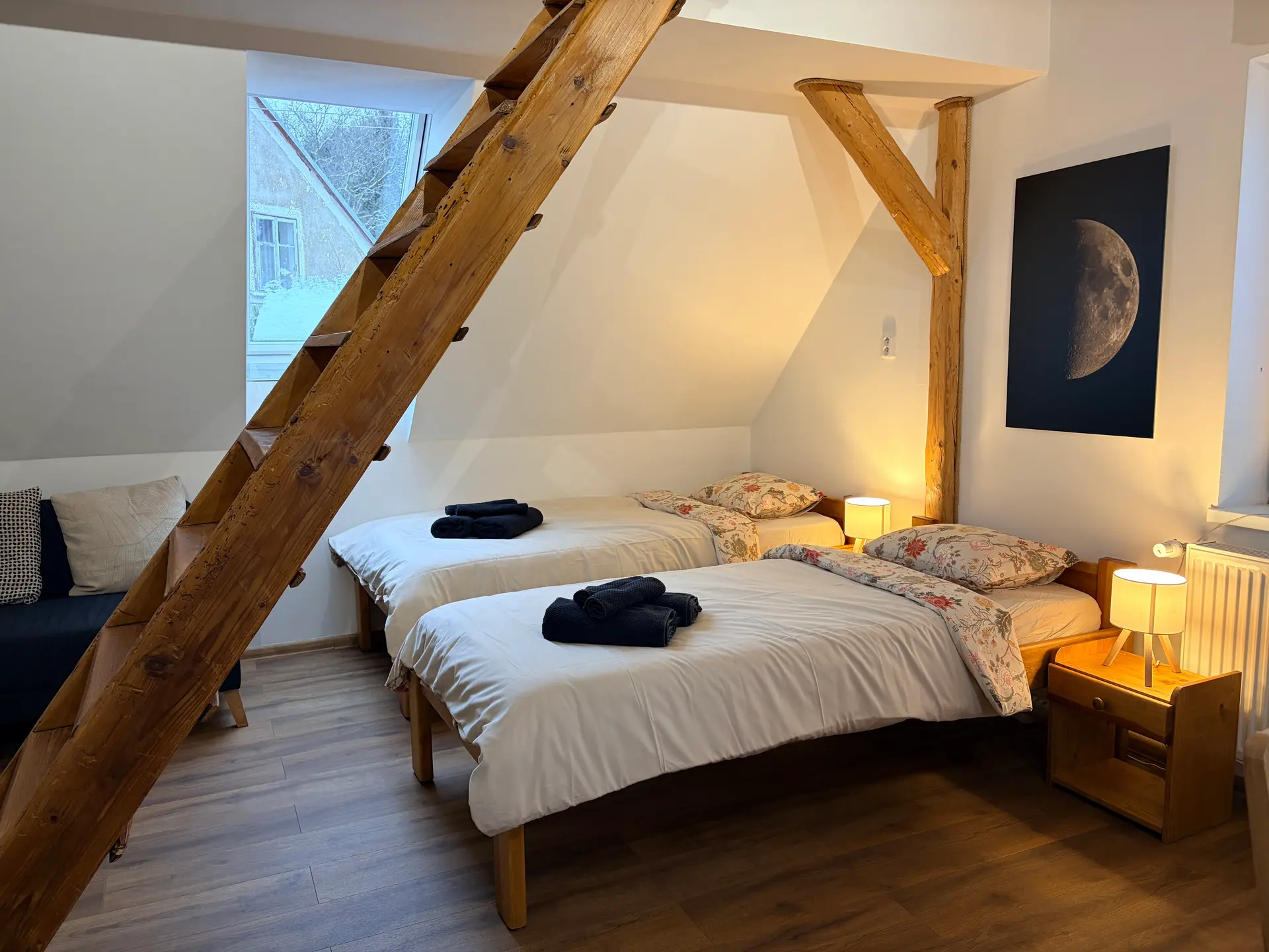 Podkrovní ložnice apartmánu 1 s večerním osvětlením a dřevěnými trámy